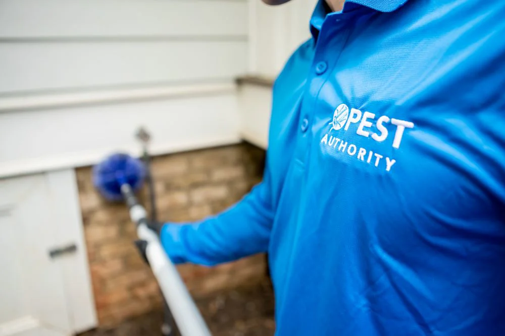 A pest control professional, wearing a blue shirt with "PEST AUTHORITY" Logo
